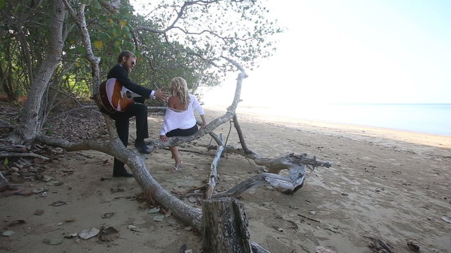 guitarist flirts with girl she sits down on branch and smiles	