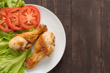 Grilled chicken legs and vegetables on wooden background.