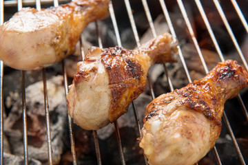 Chicken legs grilling over flames on a barbecue.
