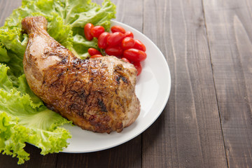 Grilled chicken legs and vegetables on wooden background.