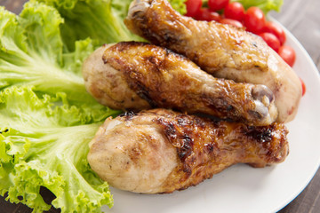 Grilled chicken legs and vegetables on wooden background.
