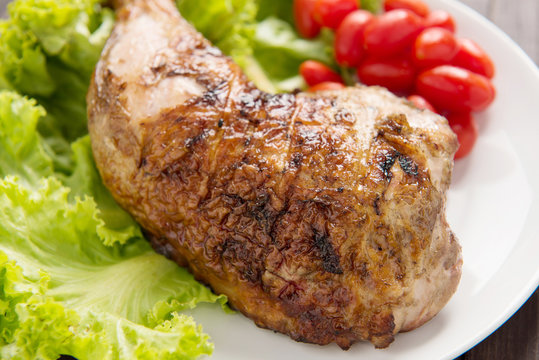 Grilled chicken legs and vegetables on wooden background.