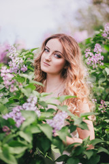 Beautiful young woman with long curly hair posing with lilacs