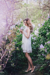 Fototapeta na wymiar Beautiful young woman with long curly hair posing with lilacs