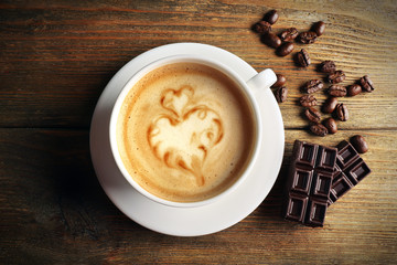 Cup of coffee latte art with grains and chocolate on wooden background