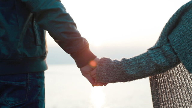 Close up of couple holding hands. Young couple in love coming closer to see sea waves
