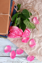 Obraz na płótnie Canvas Beautiful pink roses with stack of books on wooden table with parchment, top view