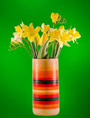 Yellow daffodils and freesias in a colored vase.