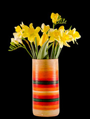 Yellow daffodils and freesias in a colored vase.