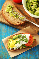 Tasty sandwich with egg, avocado and vegetables on paper napkin, on color wooden background