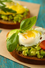 Tasty sandwich with egg, avocado and vegetables on paper napkin, on color wooden background