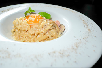 Pasta with egg yolk sprinkled with cheese on a white plate in bl