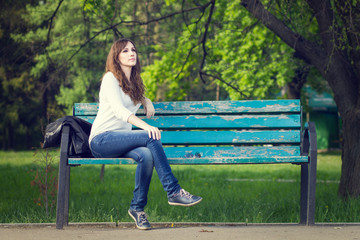 Naklejka na ściany i meble Young beautiful woman sitting on bench in park