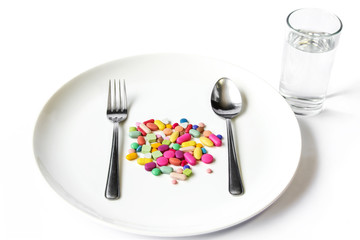 Drugs on a dish with fork , spoon and a water glass. 