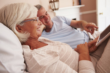 Senior Couple Lying In Bed Looking At Digital Tablet