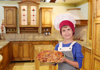 happy boy chef with pizza in kitchen