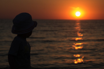 little boy standing back and enjoy the sunset on the sea

