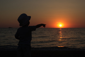 little boy standing back and watching the sunset 

