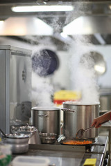 Cooking in a restaurant kitchen, steam over cooking pots - 83603504