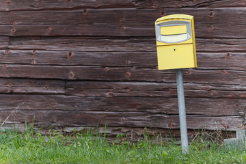 Traditional yellow postbox in front og a wooden wall
