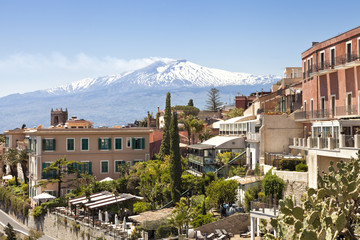 Fototapeta na wymiar Sicilian town Taormina with white peak of smoking volcano Etna