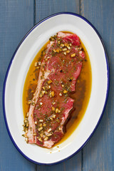 raw meat in sauce in white dish on blue wooden background
