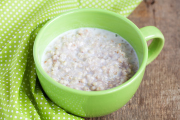 Green buckwheat porridge with milk on wooden table