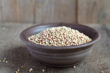 Dry green buckwheat in a clay bowl on wooden table