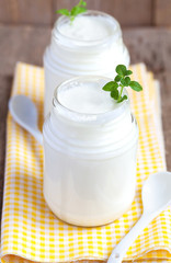 Obraz na płótnie Canvas Homemade yogurt in two small glass jars on a wooden table