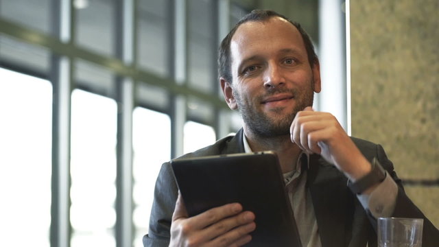 Portrait of smiling businessman with tablet computer sitting in cafe 
