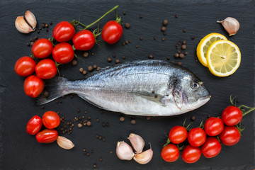 Dorado fish on slate board with cherry tomatoes, lemon, garlic