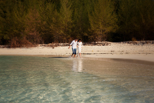 bride and groom  splash at sea edge against trees