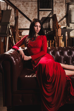 elegant sensual young woman in red dress sitting on leather sofa
