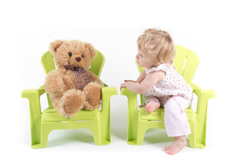 Baby Girl Sits on Green Chair and Talks with Her Toy Bear