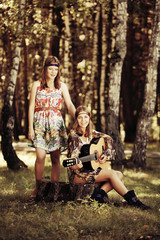 Two young fashion girls with guitar in a summer forest