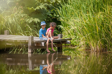 two kids fishing in a river, sitting on a wood pontoon © jackfrog