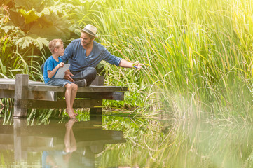 father and son using a tablet on a wooden pontoon in summertime