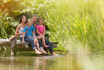 happy family sitting at the edge of a pontoon, feet in the river