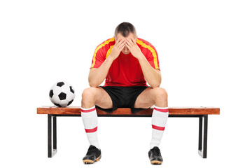 Worried young football player sitting on a bench