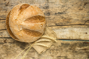 Loaf of whole wheat bread with ears on wood background