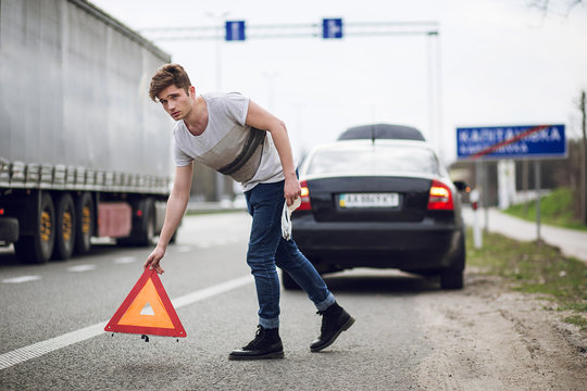 car with breakdown alongside the road, man sets warning triangle
