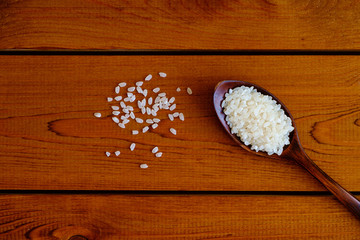 Rice grain in dark wooden spoon on wooden board, top view