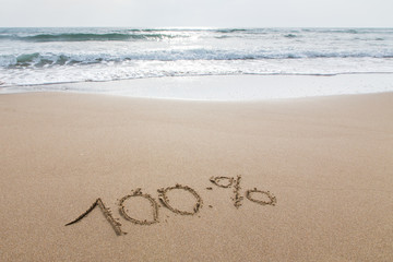 Cento percento scritto sulla sabbia in riva al mare