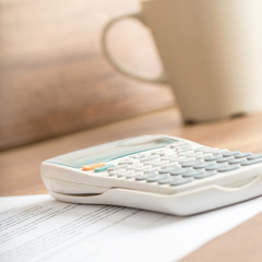 White desk calculator on a document next to a mug