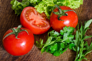 Juicy tomatoes with green-stuff on wooden table