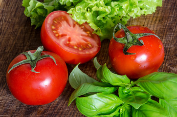 Juicy tomatoes with green-stuff on wooden table