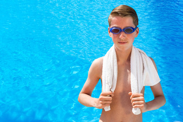Teenage boy wearing swimming goggles and towel at swimming pool