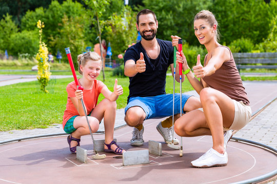 Familie spielt drau&szlig;en zusammen Minigolf