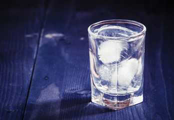 Clold fresh water with ice in a glass on a dark background in vi