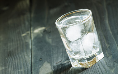 Clold fresh water with ice in a glass on a dark background in vi